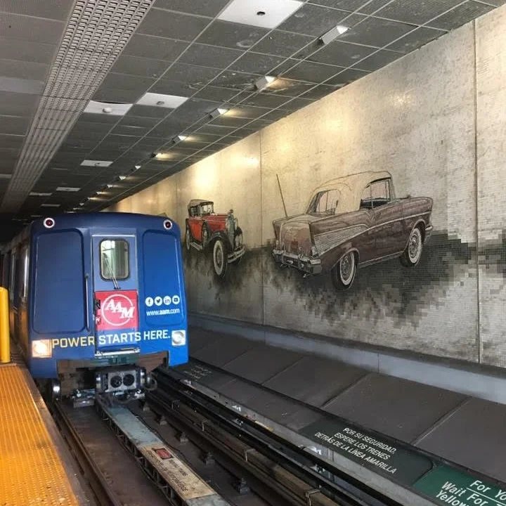 A People Mover train at a downtown station, with a mural of classic cars on the wall