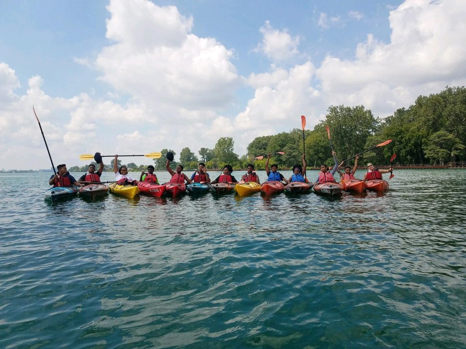 A group of kayakers raises their paddles in celebration on the Detroit River