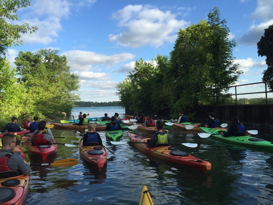 A line of colorful kayaks sets off on the water tour between the trees