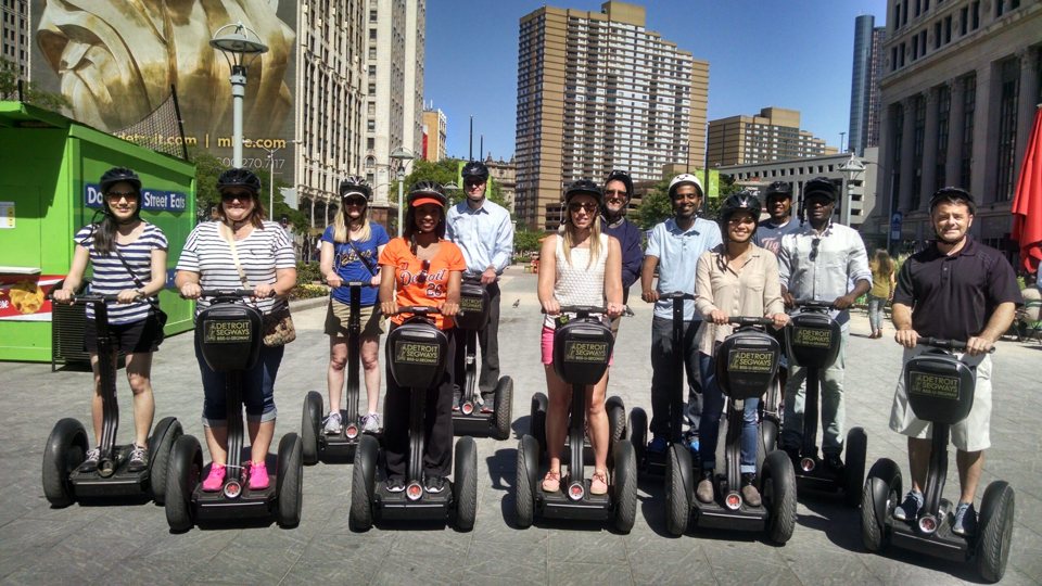 Segway-es csoport áll a Cadillac Square-en, mögötte Detroit belvárosi épületei