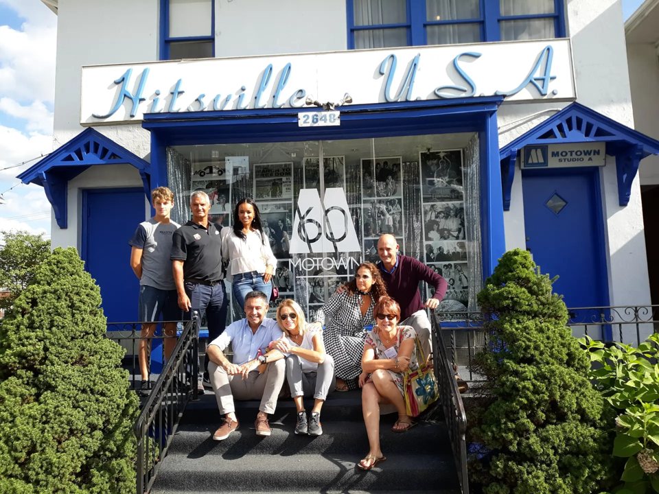 A group of tourists poses on the steps in front of the blue and white Hitsville U.S.A. Motown building