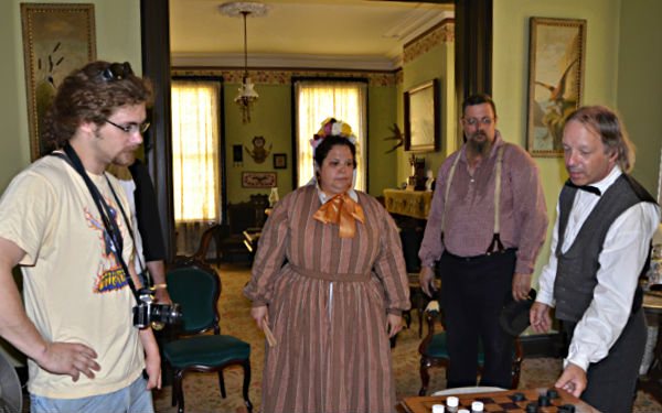 Costumed reenactors play a board game in a period-furnished parlor room