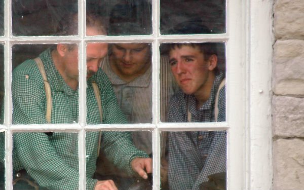 Three costumed men look out through a many-paned window