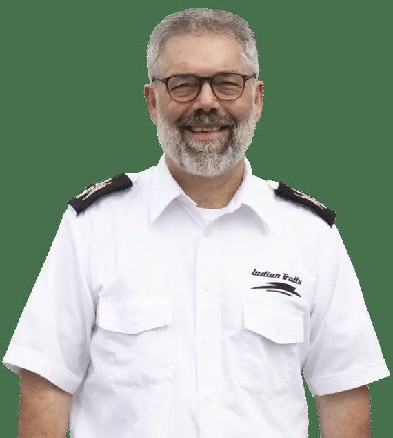 Portrait of a smiling, gray-bearded bus driver in a white uniform with the Indian Trails logo