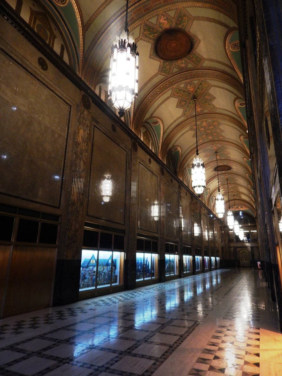 An ornately painted, arched hallway with chandeliers and checkered marble flooring in a Detroit building