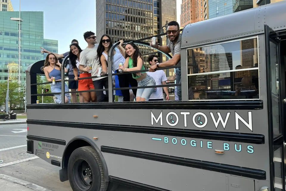 Guests dance on the open-top deck of the Motown Boogie Bus, with Detroit's skyline behind them