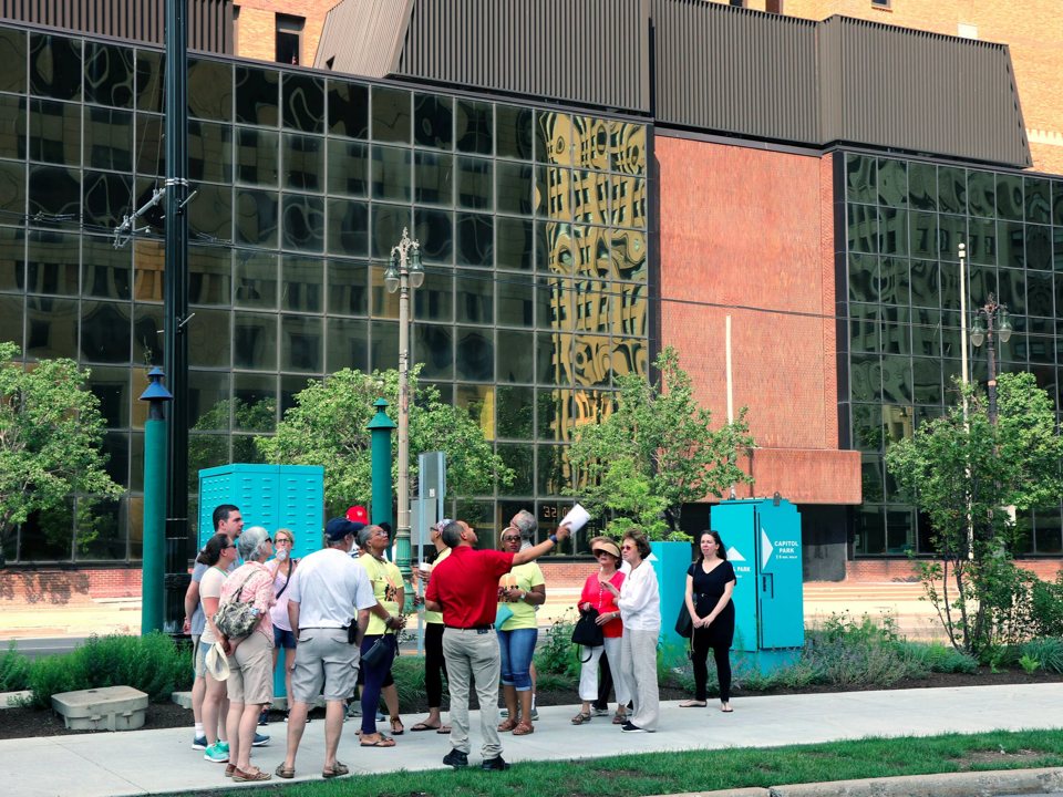 A tour group walks past a modern glass building in Detroit