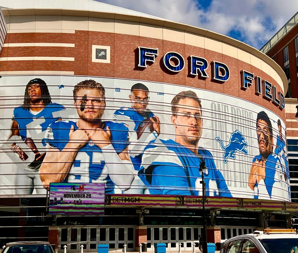 People pose in front of a large mural depicting Detroit Lions players