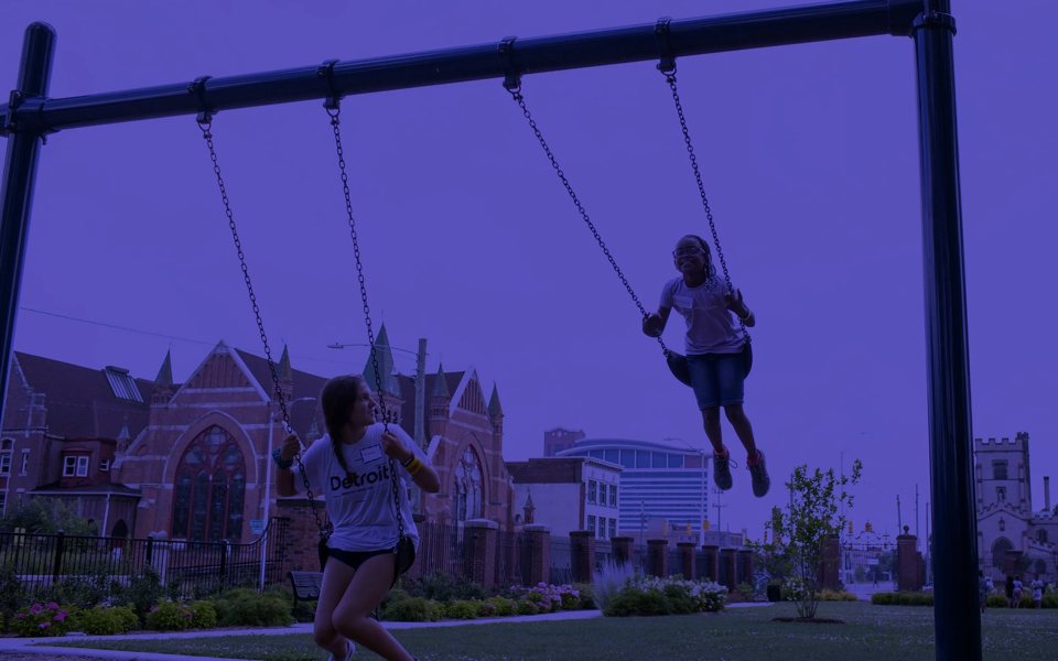 Children swing at a playground in the Woodbridge neighborhood, with a historic church behind them